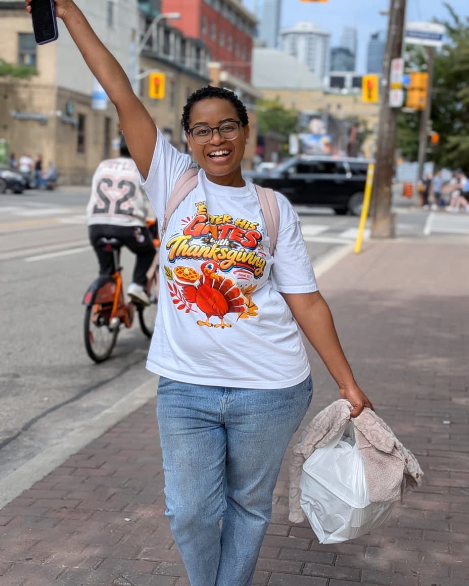 Lerato walking a city street in a BUT GOD tee, hand raised